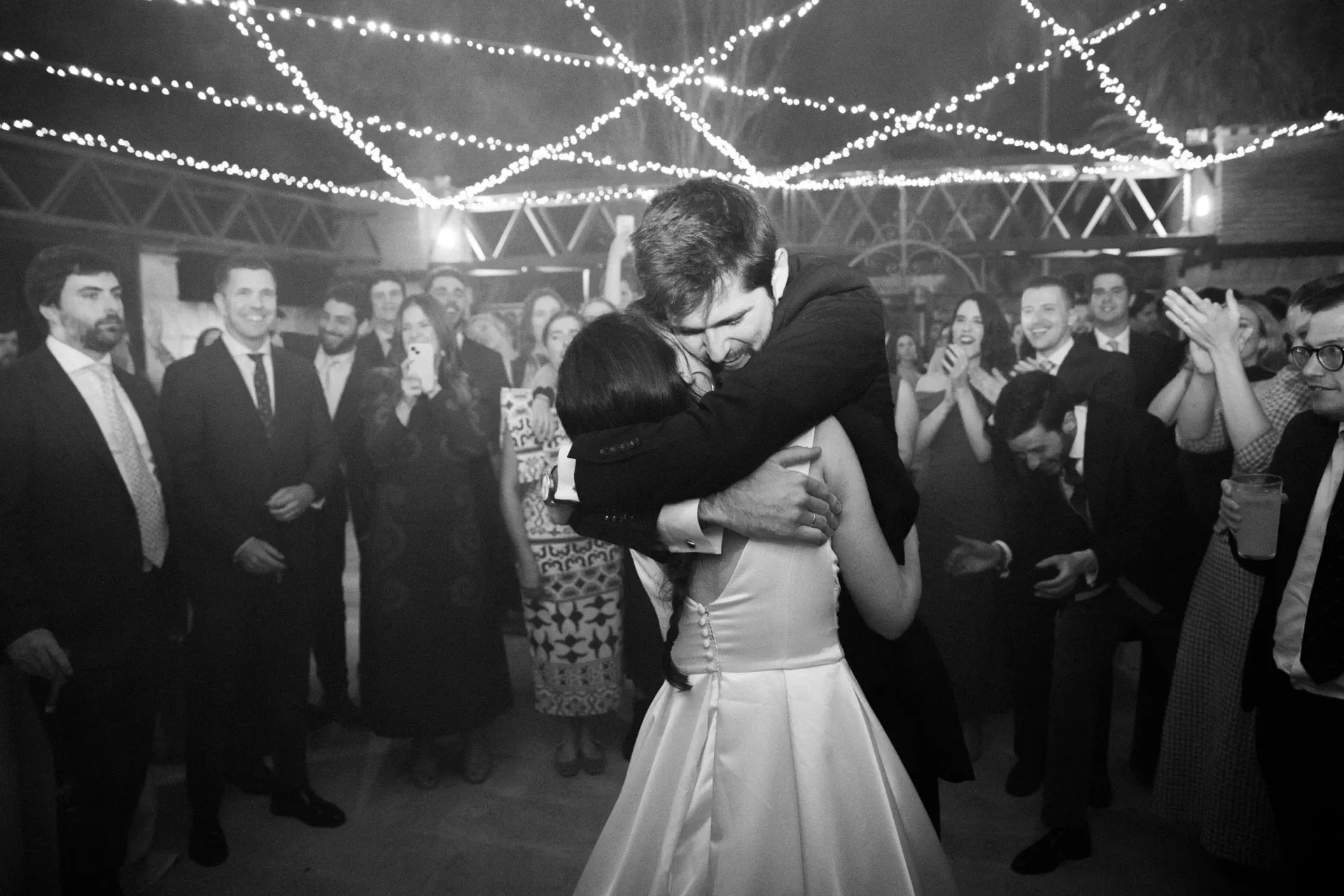 Novios abrazados en la fiesta bajo guirnaldas de luces