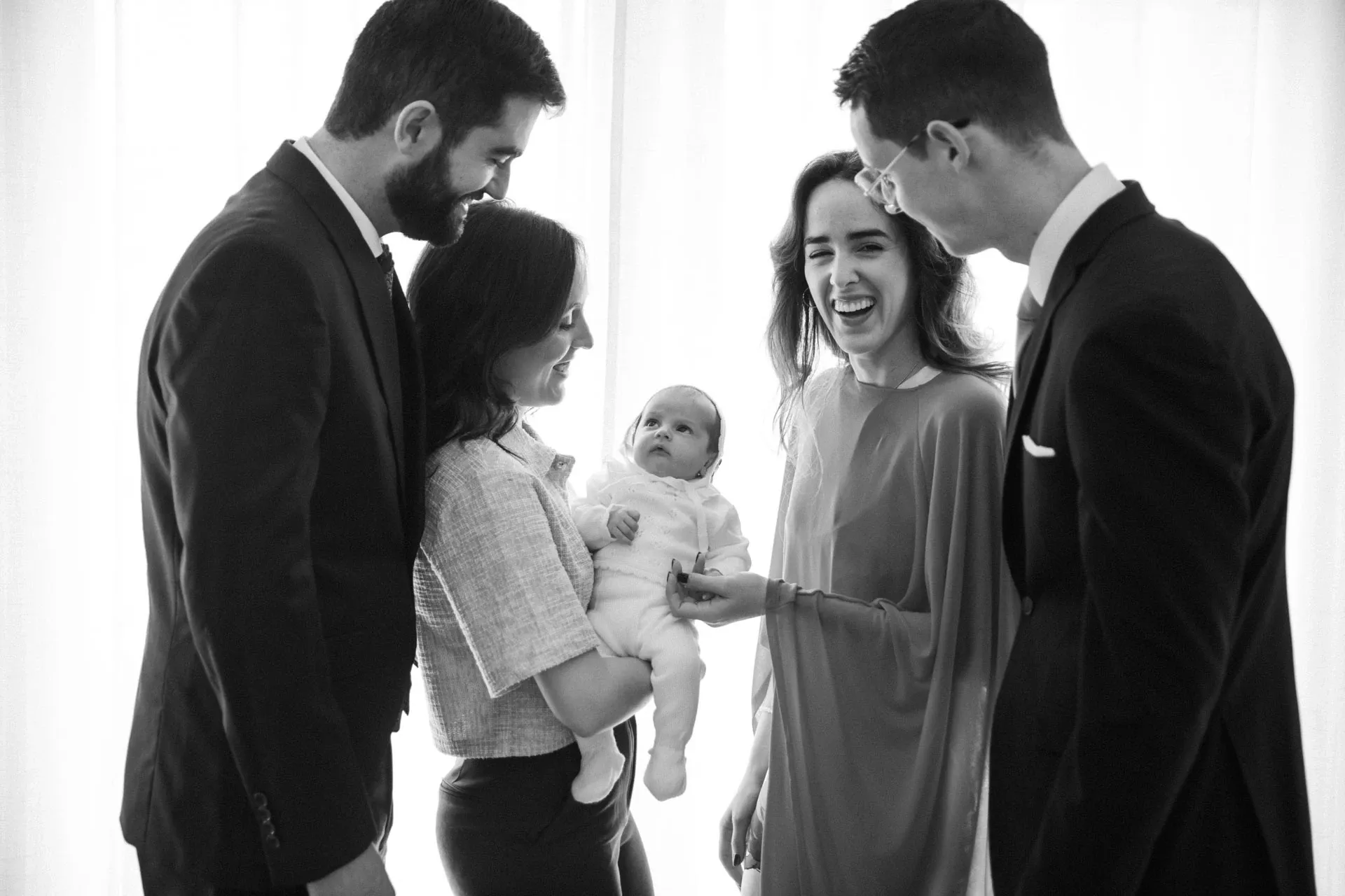 Padres y padrinos sonriendo al bebé, en blanco y negro
