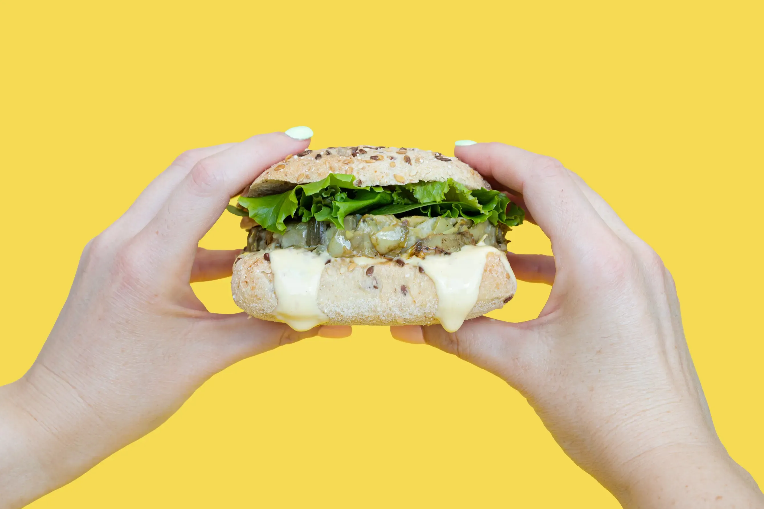 Manos sujetando un sándwich sobre fondo amarillo