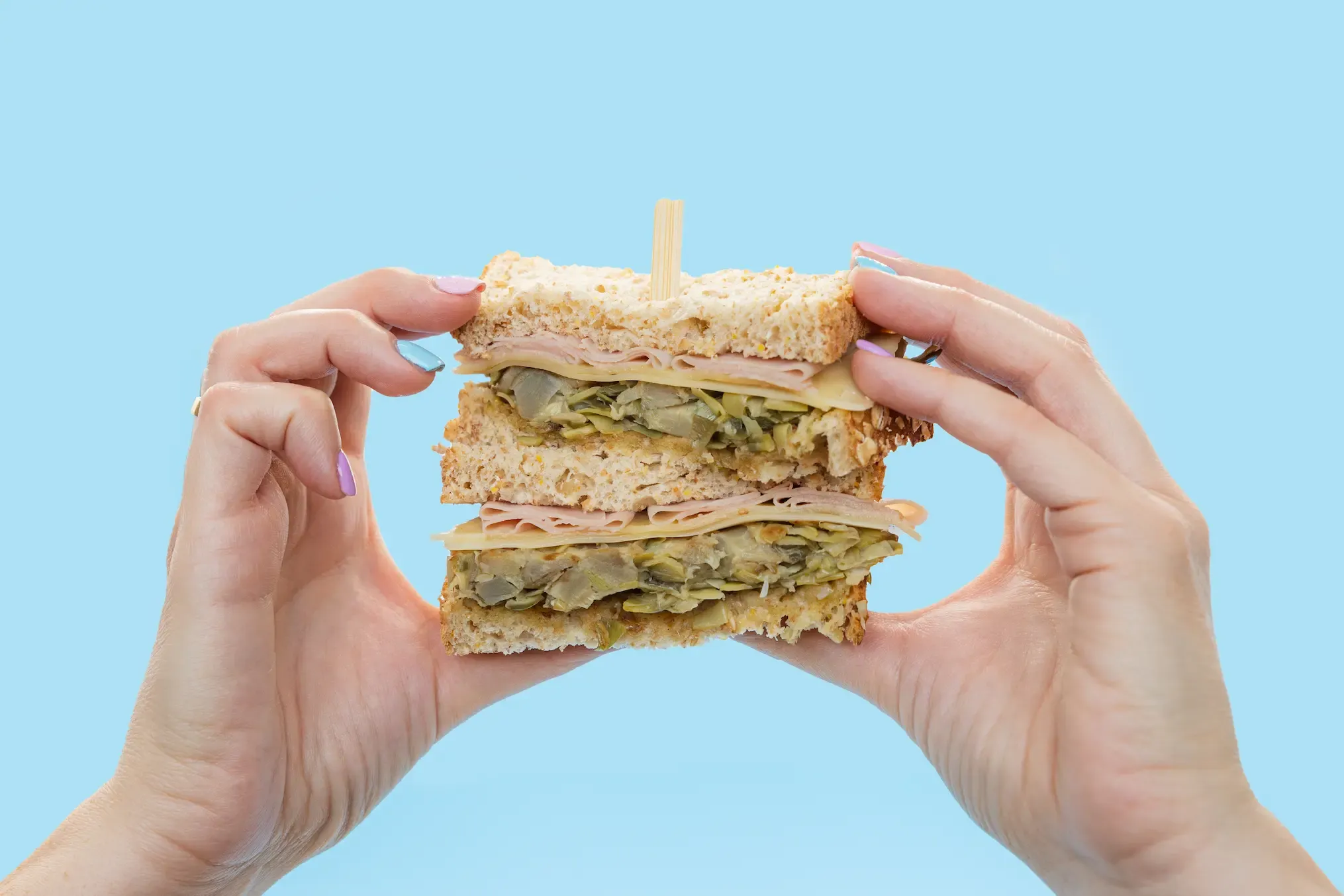Manos sosteniendo un sándwich sobre fondo azul