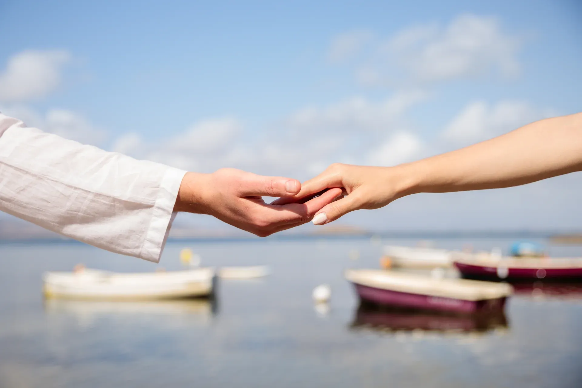 Manos de la pareja entrelazadas frente a unas barcas