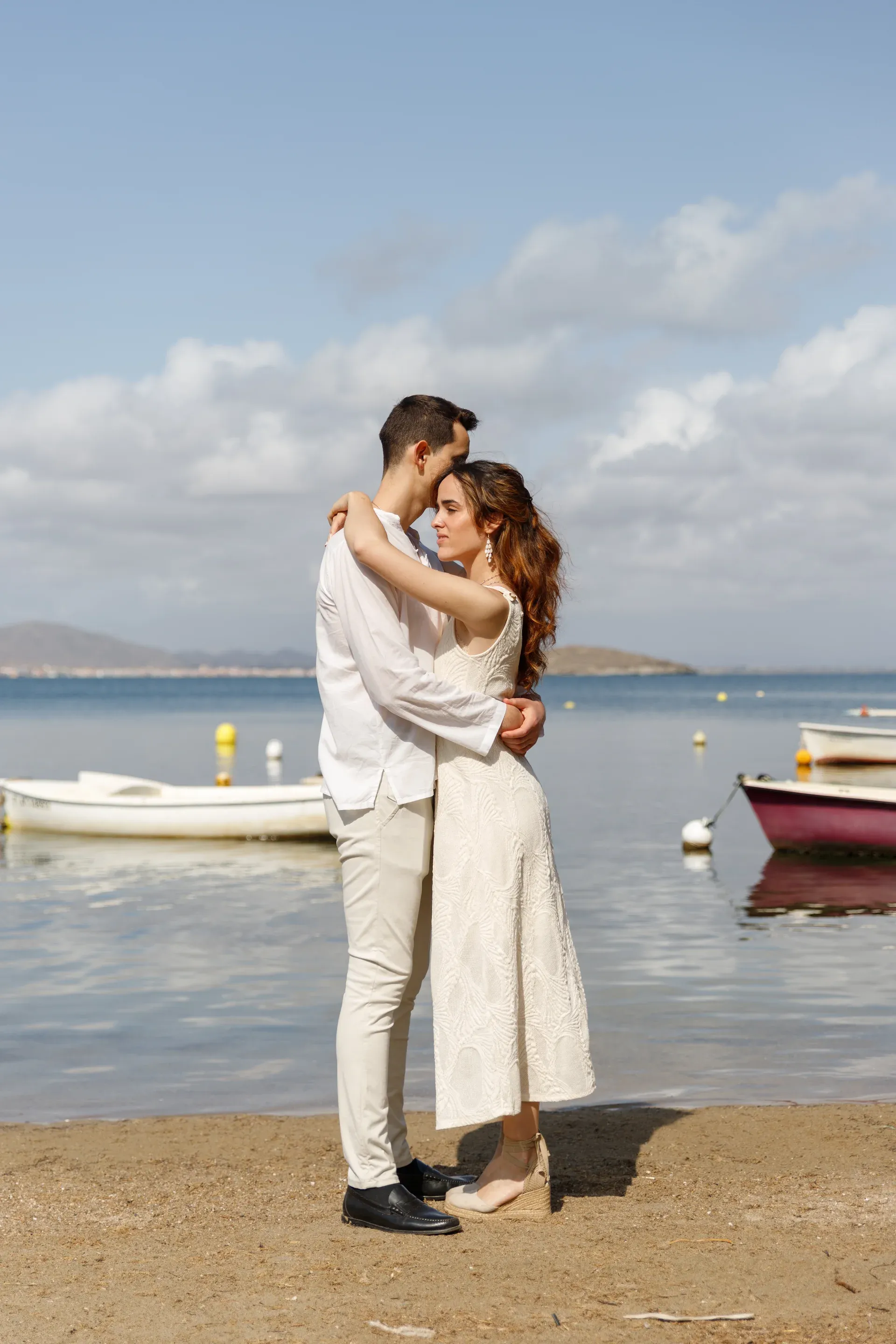 Pareja abrazada en la orilla con barcas de fondo