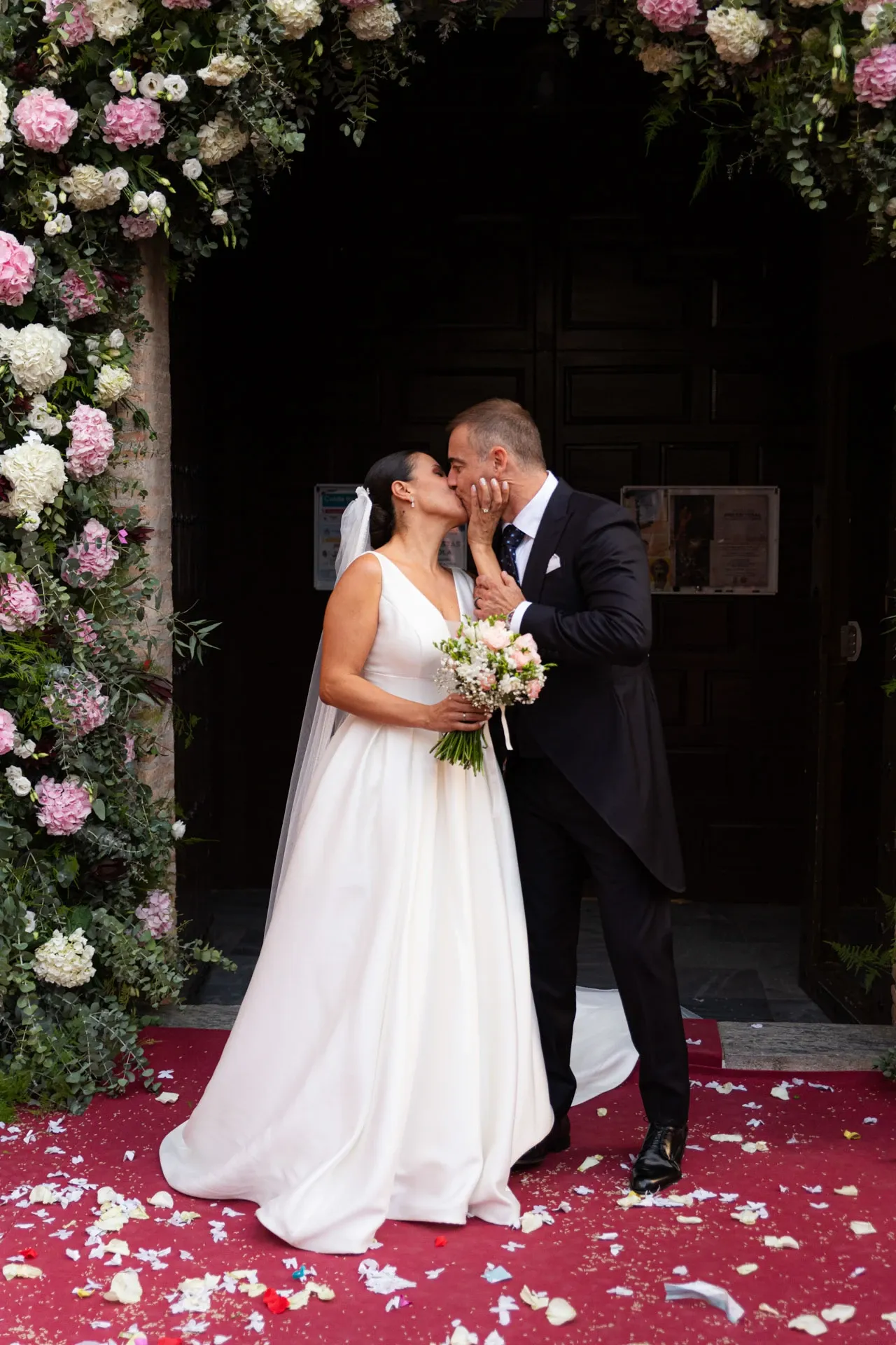 Novios besándose en la puerta de la iglesia decorada con flores